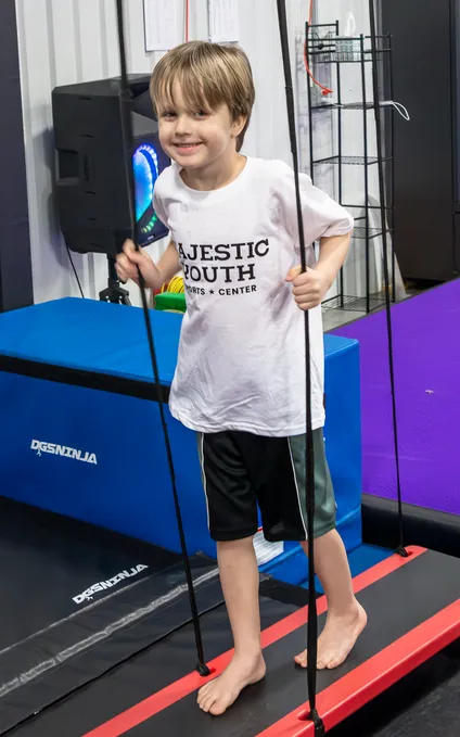 Child conquering ninja warrior obstacle course with rope climb