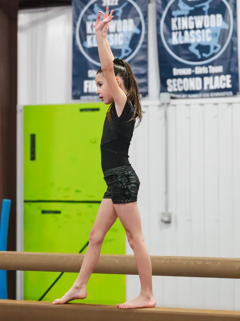 Young gymnast performing perfect form on balance beam with expert coach guidance